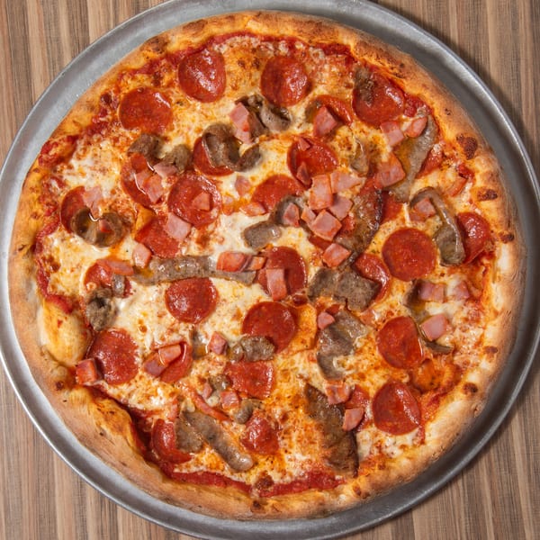 A whole meat lover's pizza with pepperoni, ham, and sausage on a metal pan.