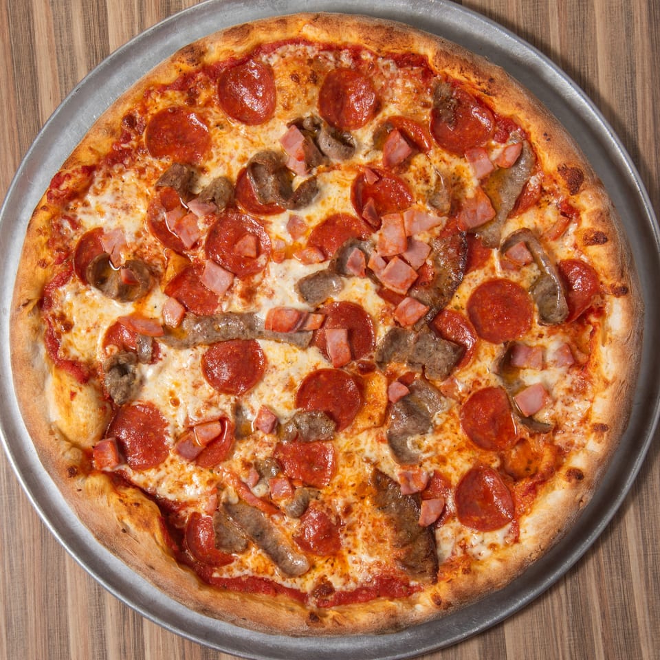 A whole meat lover's pizza with pepperoni, ham, and sausage on a metal pan.